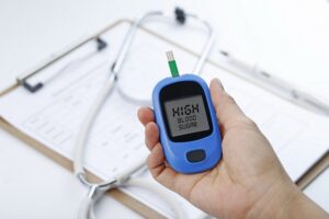 Hand holding a blood glucose meter measuring blood sugar, the background is a stethoscope and chart file